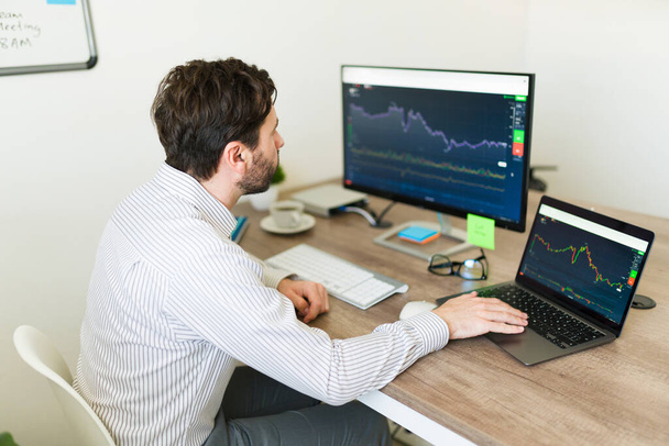 Przystojny biały mężczyzna pracuje jako makler handlowiec podczas korzystania z laptopa i komputera w biurze, aby spojrzeć na giełdzie - Zdjęcie, obraz
