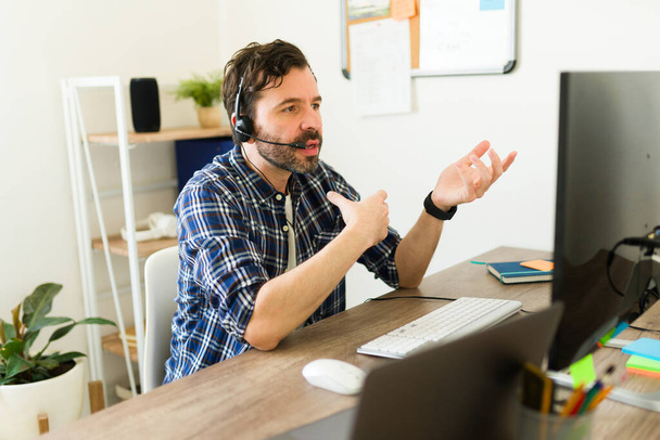 zaneprázdněný hispánský muž se sluchátky v kanceláři pracující v zákaznické podpoře nebo jako obchodní zástupce v call centru  - Fotografie, Obrázek
