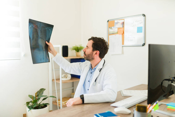 Ortopéd orvos vizsgálja az orvosi röntgenfelvételeket egy törött vagy törött csontú betegről az irodájában. - Fotó, kép