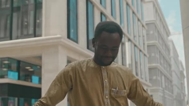 Танець веселого молодого чорношкірого танцює біля камери проти сучасної офісної будівлі в центрі міста вдень - Кадри, відео