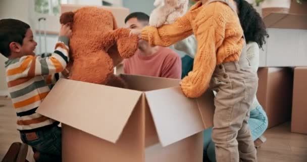 Beköltözés, játékok és családi dobozok kipakolása az új otthoni kötődésükben és közös játékukban. Boldog, mosolygós és fiatal szülők, hogy játékos játékmackó a fiú gyerekek egy modern házban - Felvétel, videó