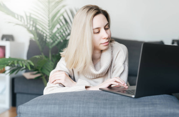 自宅でノートパソコンを使っている若い女性が居間で快適に座って.  - 写真・画像