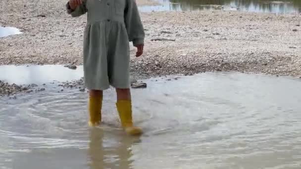 Bambina in stivali di gomma cammina attraverso una pozzanghera sulla riva del mare. Filmati 4k di alta qualità - Filmati, video