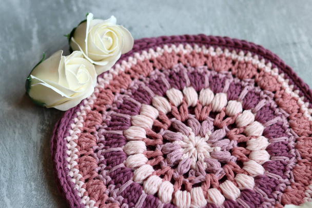 Crocheted trivet made of pink organic yarn. Handmade crochet potholder on gray background with space for text.  - Photo, Image