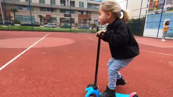 La niña monta un scooter en un campo de fútbol en el patio. Imágenes de alta calidad 4k - Metraje, vídeo