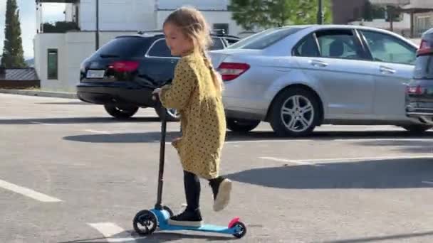 Mała dziewczynka jeździ na skuterze na parkingu z samochodami. Wysokiej jakości materiał 4k - Materiał filmowy, wideo