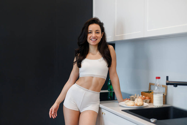 Hymyilevä seksikäs nainen poseeraa seistessään keittiössä kotona aamulla ja valmistelee aamiaista. Terveiden, kotimaisten elämäntapojen käsite. - Valokuva, kuva