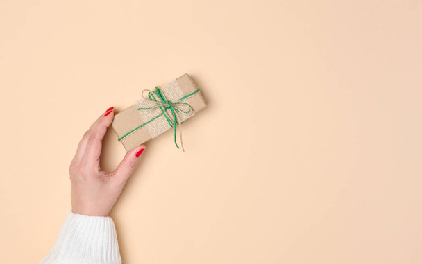 Female hand holding a gift box on a beige background. View from above - Photo, Image