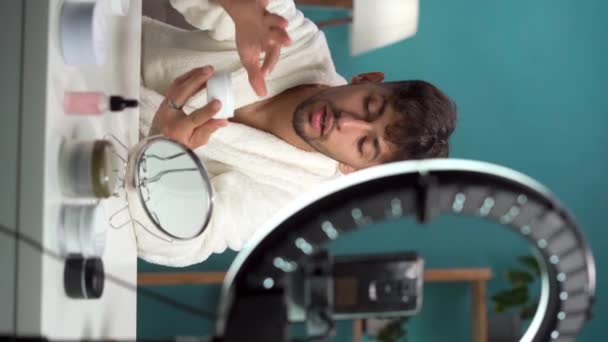 Arabskie piękno mężczyzna blogger filmowanie codziennej pielęgnacji skóry rutynowy tutorial przed kamerą. Social media influencer live streaming product review in home studio. Stosowanie kremu do twarzy na skórę męską - Materiał filmowy, wideo
