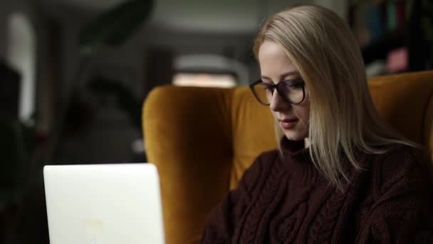 眼鏡とラップトップが付いているセーターの白人女性は自宅のアームチェアに座ります - 映像、動画