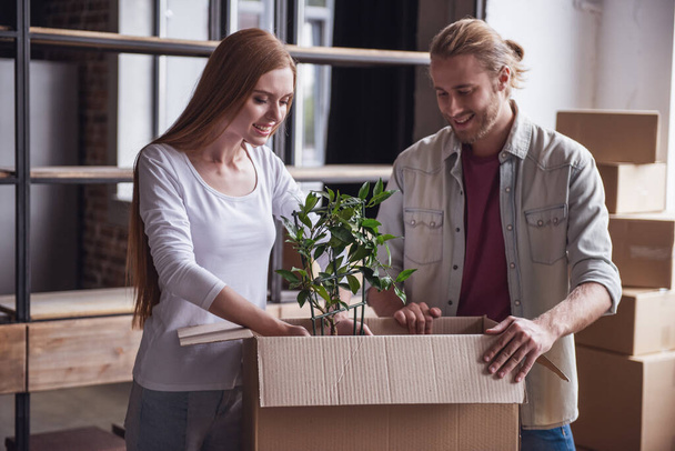 Beautiful young couple is packing their stuff into cardboard boxes and smiling while moving into new apartment - Photo, Image