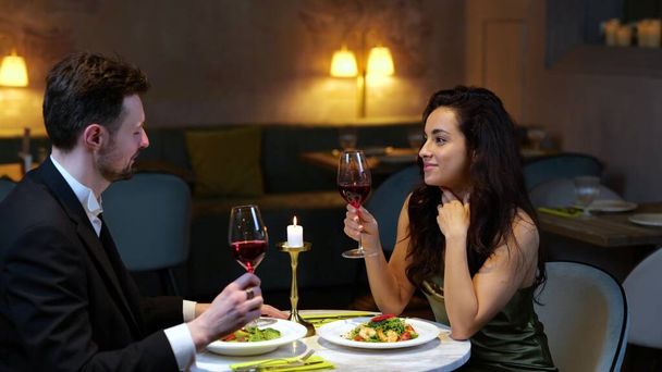 Sonriente pareja romántica tintineo con copas de vino mientras disfruta de la fecha en el restaurante. Estilo de vida, amor, concepto de relaciones. Movimiento lento - Foto, Imagen