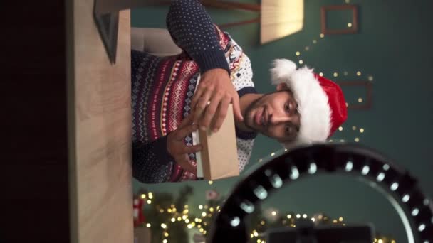 Arabic Tech vlogger robi rozpakowywanie recenzję wideo smartfona, prezentując online. Social media influencer noszenie Santa kapelusz rozpakowywanie telefonu komórkowego podczas nagrywania transmisji na żywo. Pionowe wideo - Materiał filmowy, wideo