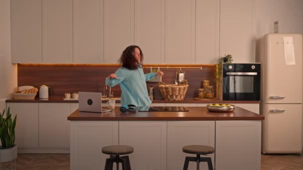 aufgeregte Frau mit langen lockigen Haaren tanzt lustig in der heimischen Küche - Filmmaterial, Video