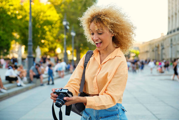 Brazilian female tourist laughing and looking at photos in her camera while sightseeing in Madrid, Spain. - Photo, Image