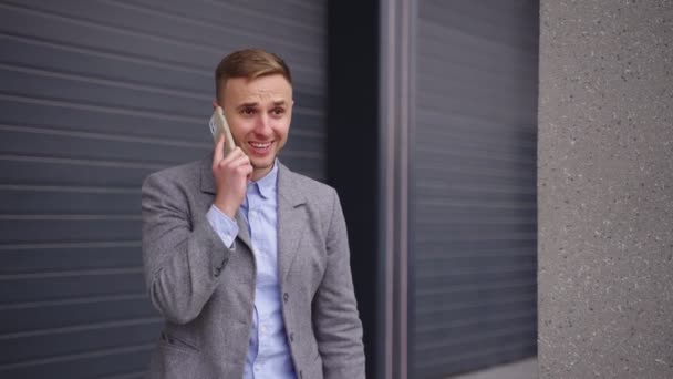Happy young businessman standing outdoors and talking on the mobile phone, celebrating success. Business, technology concept. Slow motion - Footage, Video