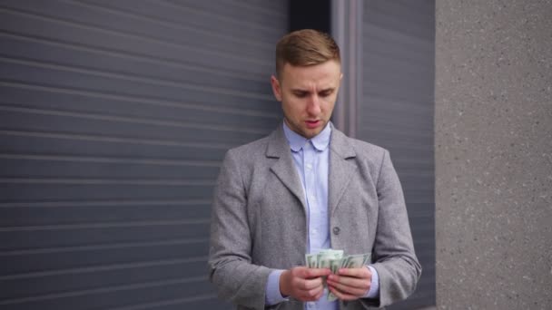 Young man standing outdoors and counting money, putting in the pocket. Copy space. Business, payment concept. Slow motion - Footage, Video