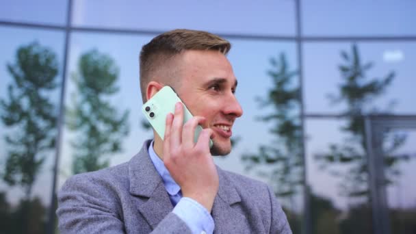 Lächelnder junger Geschäftsmann, der draußen steht und sein Smartphone benutzt, um zu reden. Business, Technologiekonzept. Zeitlupe - Filmmaterial, Video