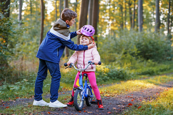 School kid boy, brother put on little preschool sister girl bike helmet on head. Brother teaching happy child cycling and having fun with learning bike. Active siblings family outdoors. Kids activity. - Photo, Image