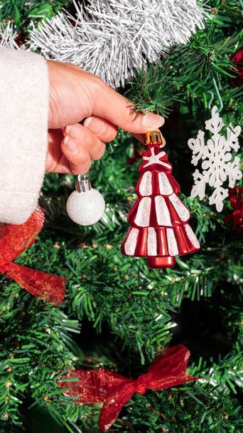 Азиатка украшает елку красивым современным элементом. Девушка украшена праздничными рождественскими украшениями. Новогодний элемент дизайна - Фото, изображение