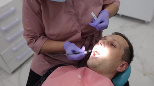 Dentista di primo piano che esamina il paziente maschio con strumenti in clinica dentale - Filmati, video