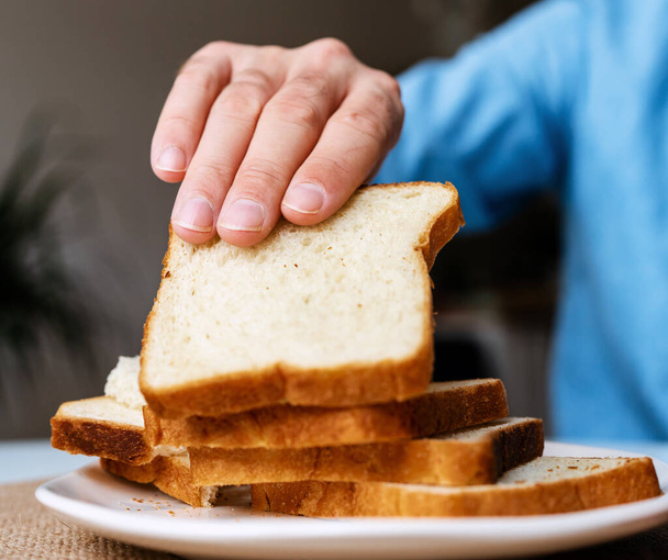 Мужская рука берет кусок хлеба для тоста. - Фото, изображение