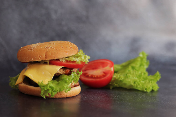 Doppelter Cheeseburger und Gemüse auf grauem Hintergrund. Saftige leckere Burger aus nächster Nähe, Seitenansicht. Fast food. Kopierraum - Foto, Bild