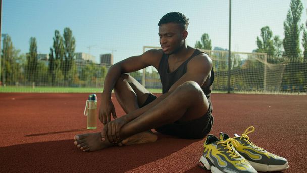 Szomorú rosszul afro-amerikai férfi sportoló futó sportoló futballista szenved fájdalmas sérült láb a stadionban úgy érzi, fáj izomgörcs bőrkeményedés fájdalom fáj sport trauma edzés láb sérülés a városban szabadban - Fotó, kép