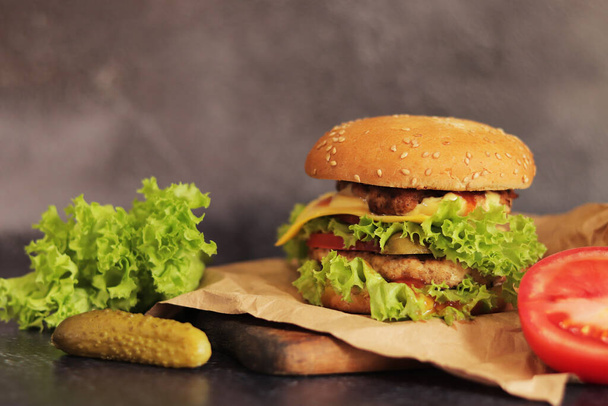 Double cheeseburger and vegetables on a gray background. Juicy tasty burger close-up, side view. Fast food - Photo, Image