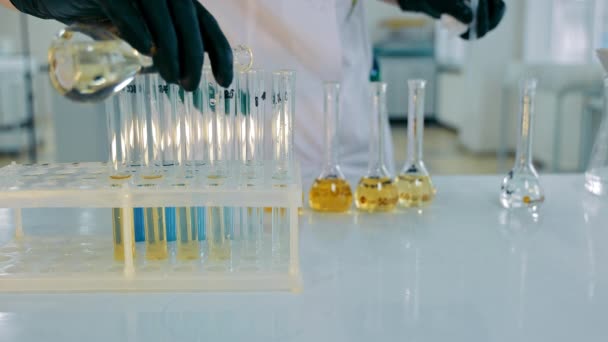 Ein Wissenschaftler gießt während eines Laborexperiments eine chemische Lösung in ein Reagenzglas. Laborexperimente: Eine gelbe Flüssigkeit wird aus einem Kolben in Reagenzgläser gegossen. Medizinische Forschung, Analyse. Schließen - Filmmaterial, Video