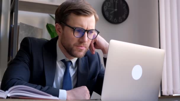 Üzletember ül az asztalnál üzleti öltönyben nézi laptop képernyőn gondolkodás pénzügyi befektetési döntés az irodában. - Felvétel, videó