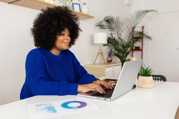 Boldog fiatal üzletasszony, aki laptopot használ otthon. Afrikai profi női dolgozó dolgozik számítógép ül az asztalon a nappaliban. Üzleti koncepció. - Fotó, kép