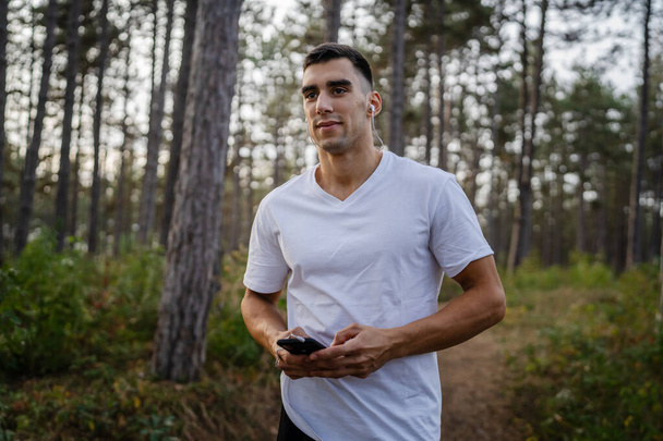 Портрет спортсмена с помощью мобильного телефона во время утренней пробежки Атлетик слушает музыку на наушниках с помощью приложения мобильного телефона - Фото, изображение