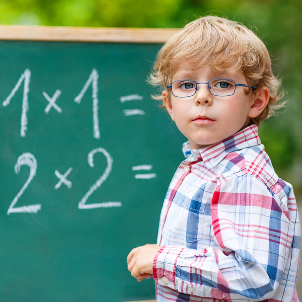 Preschool kid boy with glasses at blackboard practicing mathemat - 写真・画像