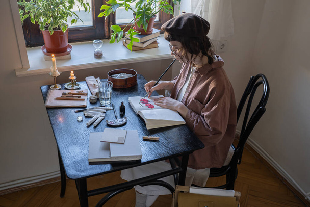 Freelance animator sitting at table and sketching in art school, workshop. Illustrator creating animation. Drawing tutor working at master class. Artist tools, paints, sketch book lying on table - Photo, Image