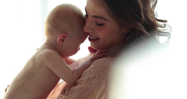 Krásná matka drží v náručí malé nahé dítě. Mladá matka s krásným účesem a make-upem drží dítě v náručí. Detailní záběr, zpomalení - Fotografie, Obrázek