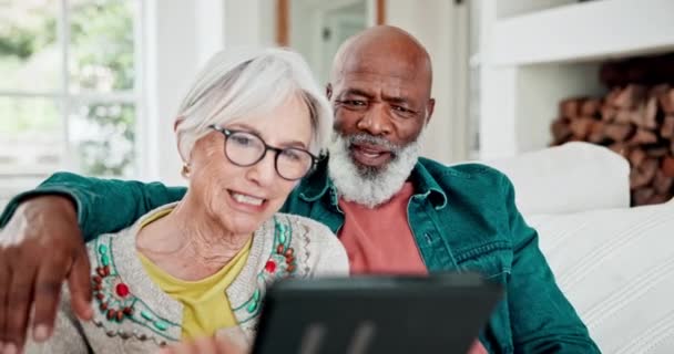Old couple on sofa with tablet, conversation and relax with love, interracial marriage or bonding in home. Social media meme, digital app and smile, senior man and happy woman on couch in living room. - Footage, Video