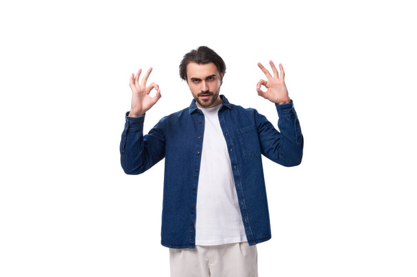 handsome young brunette man in a denim shirt gesturing with his hands on a white background. - Photo, Image