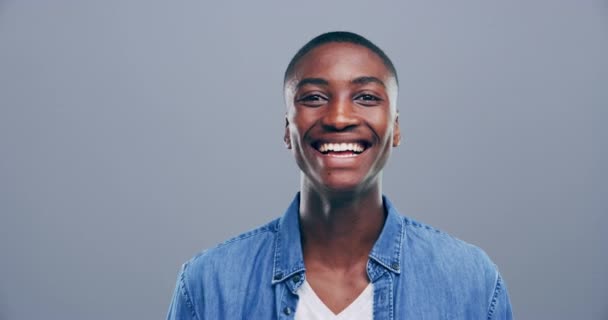 Laughing, wink and face of black man in studio for confidence, flirting and romance on gray background. Happy, body language and portrait of African person with reaction for secret, comic and emoji. - Footage, Video