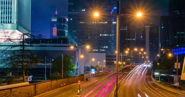 Hongkongin katuliikenne yöllä timelapse. Toimisto pilvenpiirtäjä rakennuksia ja vilkas liikenne valtatie tiellä hämärtynyt autoja valo polkuja. Hong Kongissa, Kiinassa. Kamera zoom voimassa - Materiaali, video