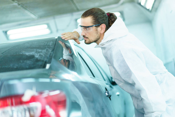 Professional automotive painting technician in chemical protecting suit inspecting car painting quality in painting chamber together. Car painting and detailing technicians portrait. - Φωτογραφία, εικόνα