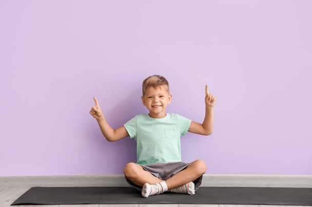 Küçük çocuk yoga minderinde oturuyor ve leylak duvarına bir şey doğrultuyor. - Fotoğraf, Görsel