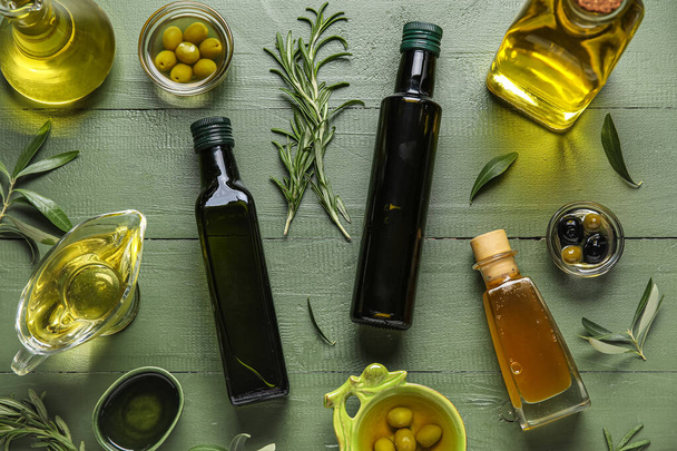 Різний скляний посуд зі свіжою оливковою олією на зеленому дерев'яному фоні - Фото, зображення