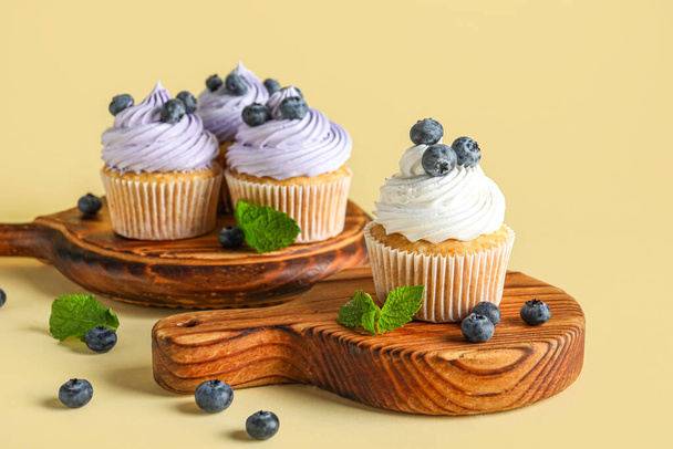 Wooden boards of tasty cupcake with blueberries on yellow background - Photo, Image