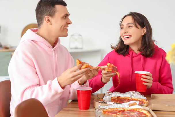 Giovane coppia mangiare gustosa pizza al salame piccante in cucina - Foto, immagini