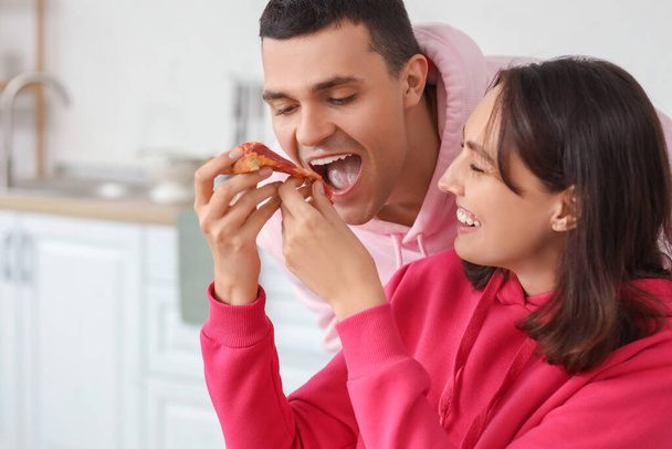 Coppia giovane che mangia gustosa pizza al salame piccante in cucina, primo piano - Foto, immagini