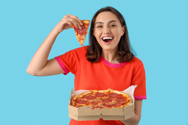 Mujer joven con sabrosa pizza de pepperoni sobre fondo azul - Foto, Imagen