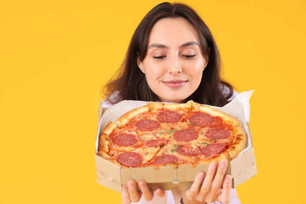 Mladá žena s chutnou pepperoni pizza na žlutém pozadí, detailní záběr - Fotografie, Obrázek