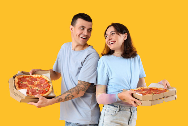 Pareja joven con sabrosa pizza de pepperoni sobre fondo amarillo - Foto, imagen