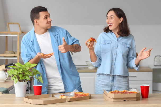 Νεαρό ζευγάρι τρώει νόστιμη πίτσα πεπερόνι στην κουζίνα - Φωτογραφία, εικόνα